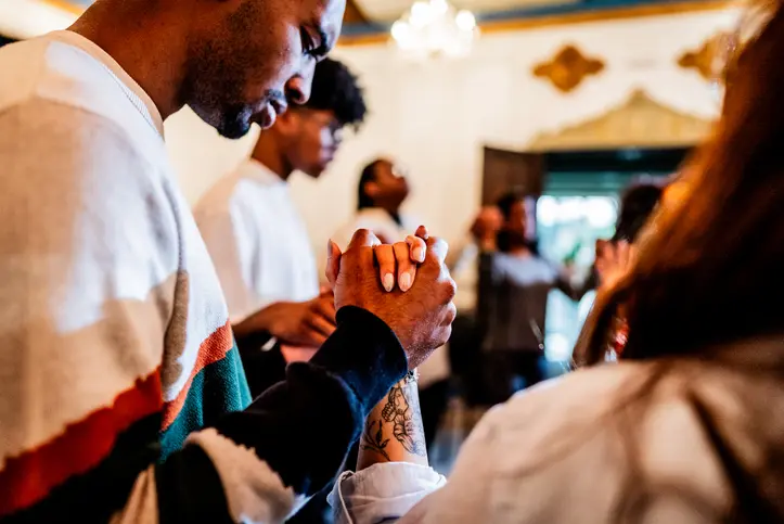 People praying together with hands clasped in a warm, communal setting.