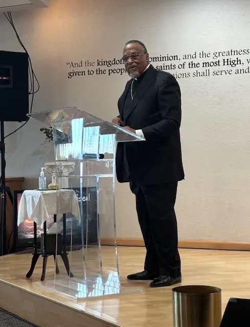 A man in a suit speaking at a podium in a church setting.