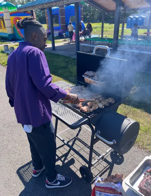 Person grilling meat outdoors with smoke rising.