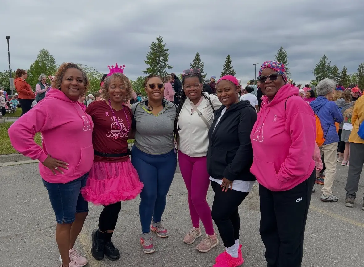 A group of six women dressed in pink and casual wear outdoors.