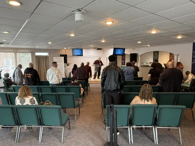 People gathered in a room with chairs and screens, possibly for a meeting or event.