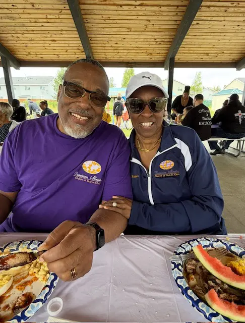 Two people smiling at an outdoor picnic under a covered pavilion.