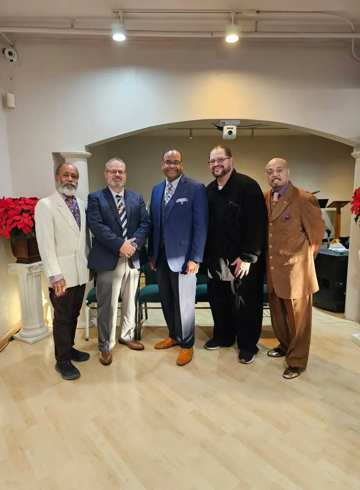 Five men dressed in formal attire posing in a room with festive decorations.