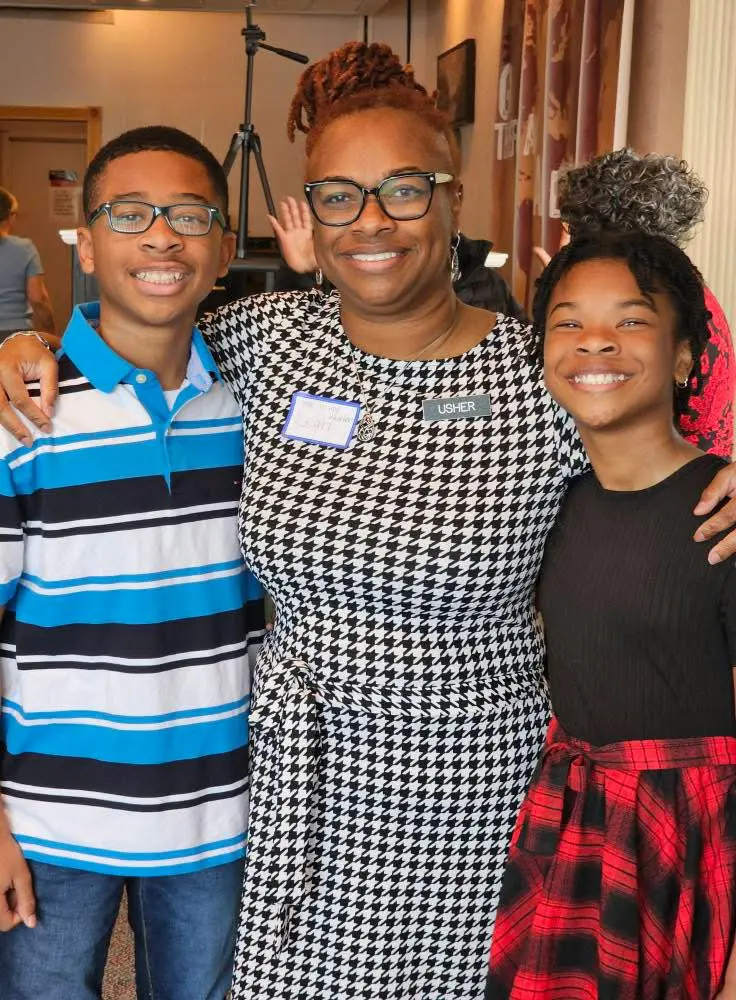 A smiling woman with two children posing together indoors.