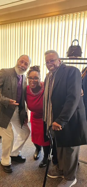 Three people smiling indoors, dressed in formal and semi-formal attire.
