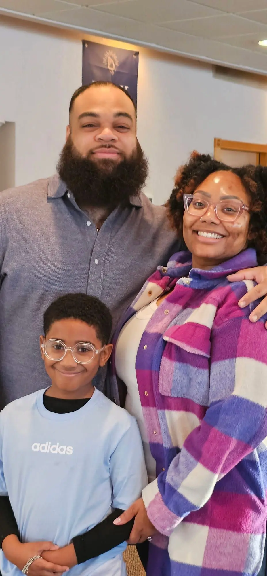 A smiling family portrait with a bearded man, a woman in glasses and a plaid shirt, and a young boy.