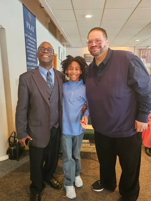 Three people smiling and posing together indoors.