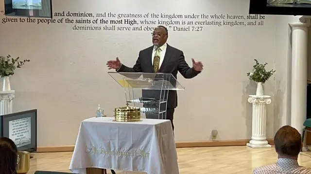 Man preaching passionately at a church pulpit with scripture on the wall.
